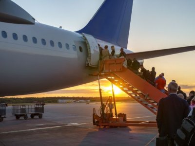 people in a line going up stairs to a plane door with the sun setting in the background